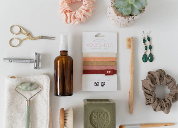 A flatlay of sustainable personal care products including a pack of Kooshoo hair ties, in tones of orange, green, and brown.