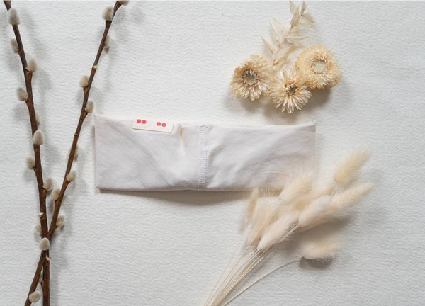 A flatlay of a white Kooshoo headband next to natural materials like pussywillow branches, brown grasses and dried flowers.