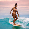 women surfing mal down wave in hawaii with her hair in high bun with luminous yellow twist headband