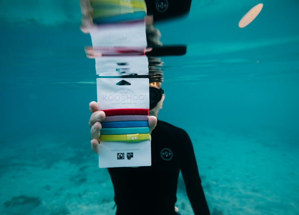 A model swims underwater holding a pack of KOOSHOO organic, plastic-free hair ties.