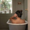 Girl sitting in bath with brown hair in high bun purple hair tie from earth tints pack