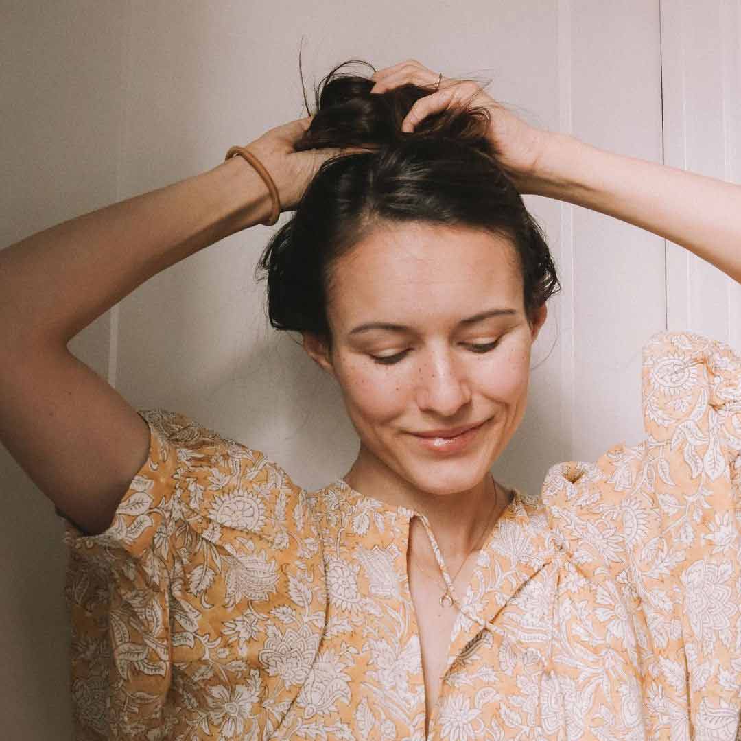 Brunette woman with high messy bun wearing KOOSHOO golden fibres hair tie around wrist