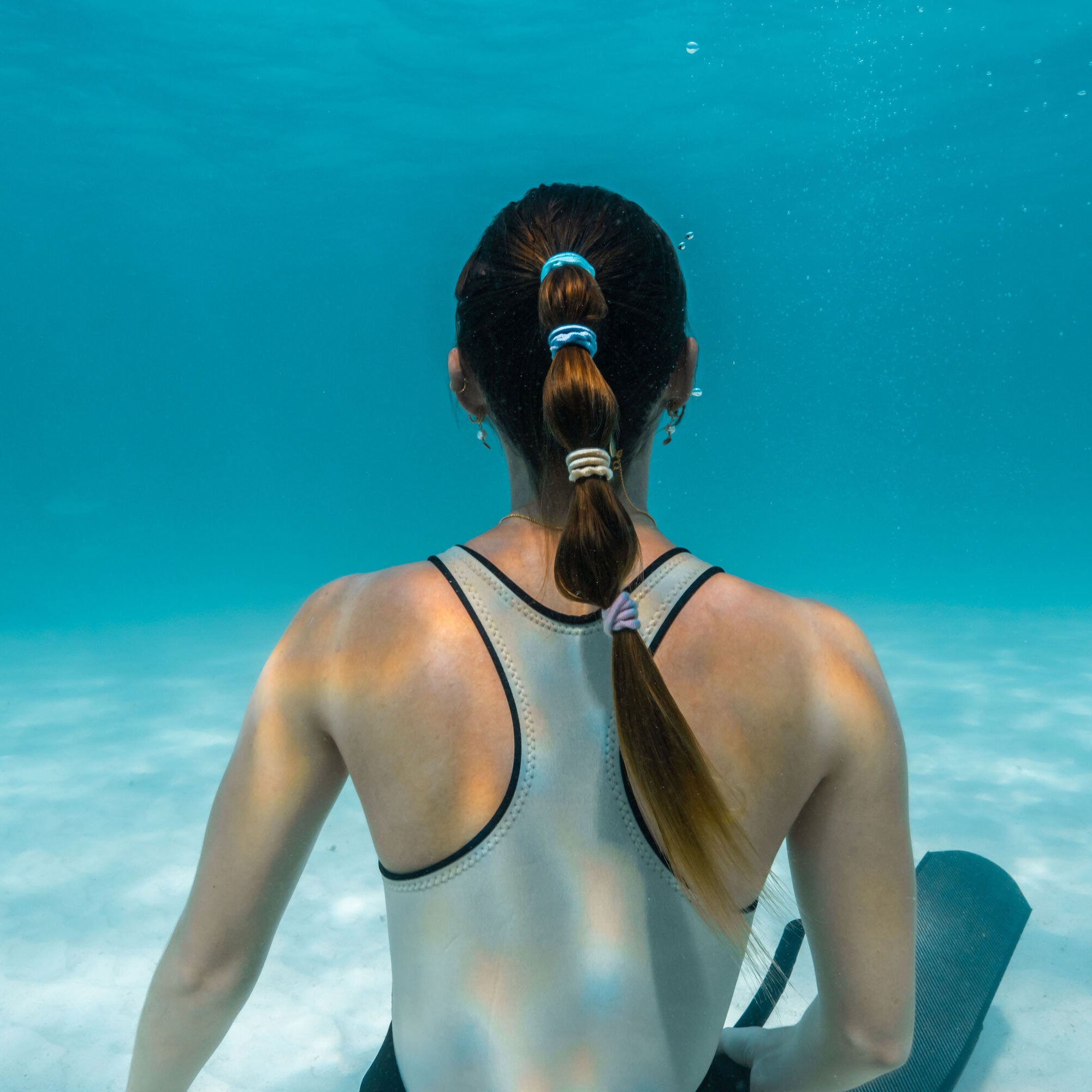 Girl underwater in the ocean with her hair in a high pony tail with pastel blooms hair tie all the way down