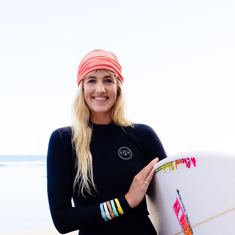 KOOSHOO organic twist headband in bright pink sugar coral. Worn on blond surfer girl with white quad fin surfboard #color_sugar-coral